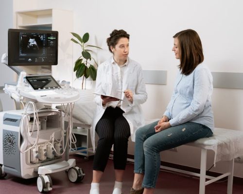Healthcare professional consulting with a pregnant patient in a medical clinic using ultrasound equipment.